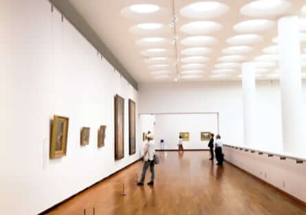 Gallery room displaying a collection of paintings with individuals admiring the artwork